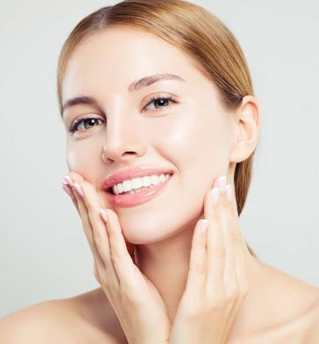 Smiling woman gently touching her face.