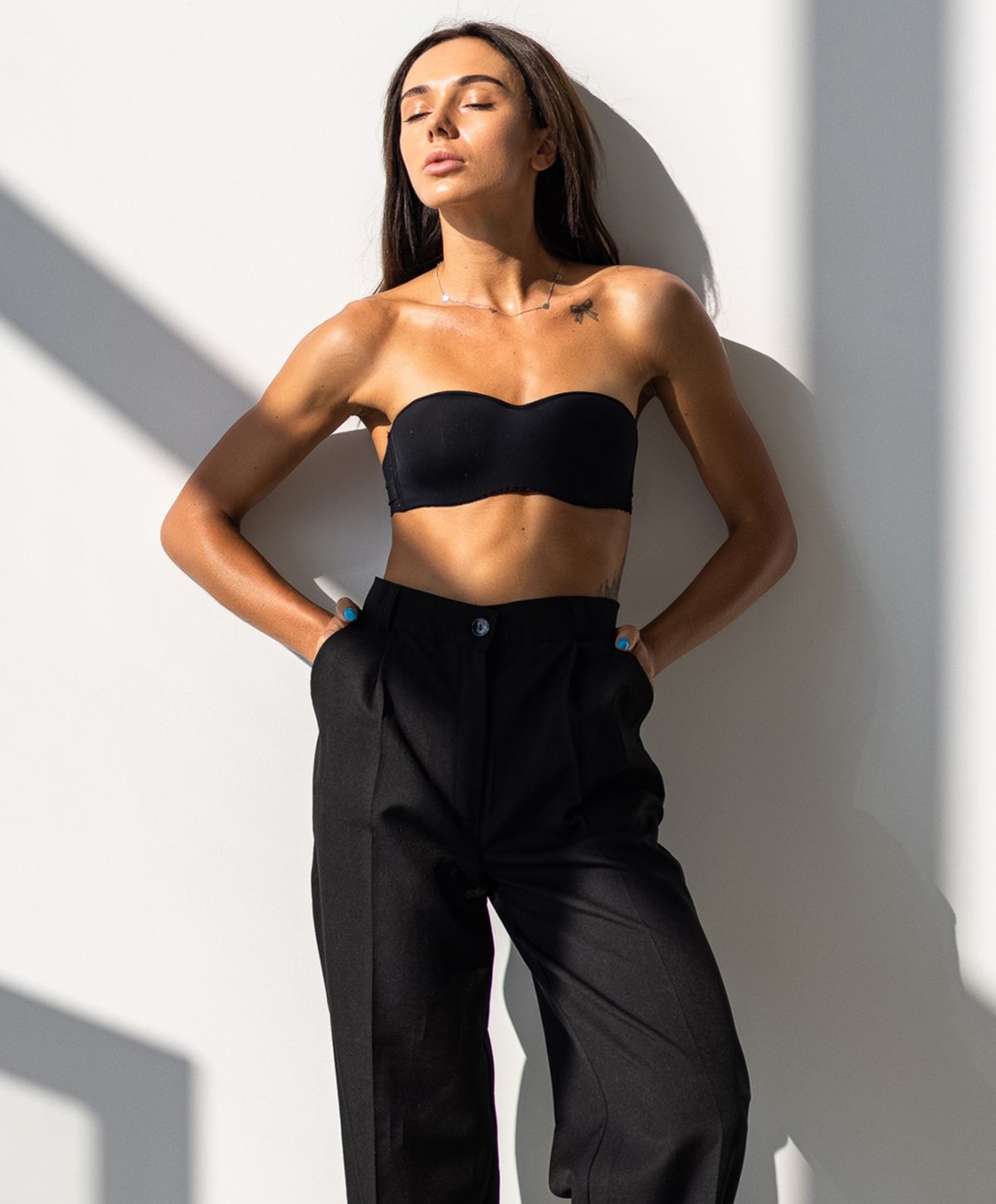 Woman posing in black outfit against white wall.