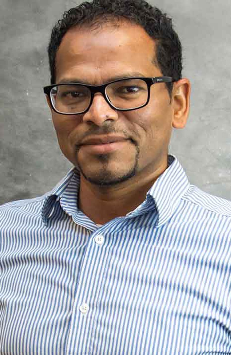 Man with glasses smiling in striped shirt.