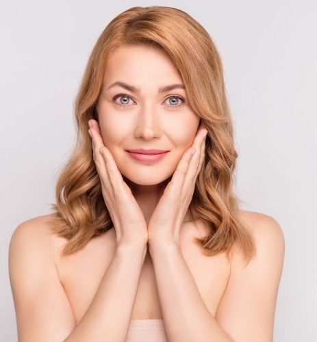 Smiling woman gently touching her face.