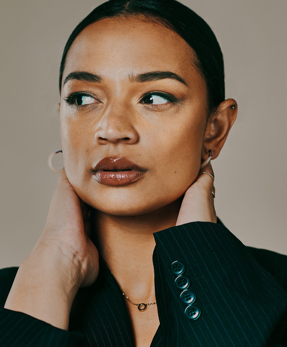 Woman in a pinstripe blazer, touching her neck.