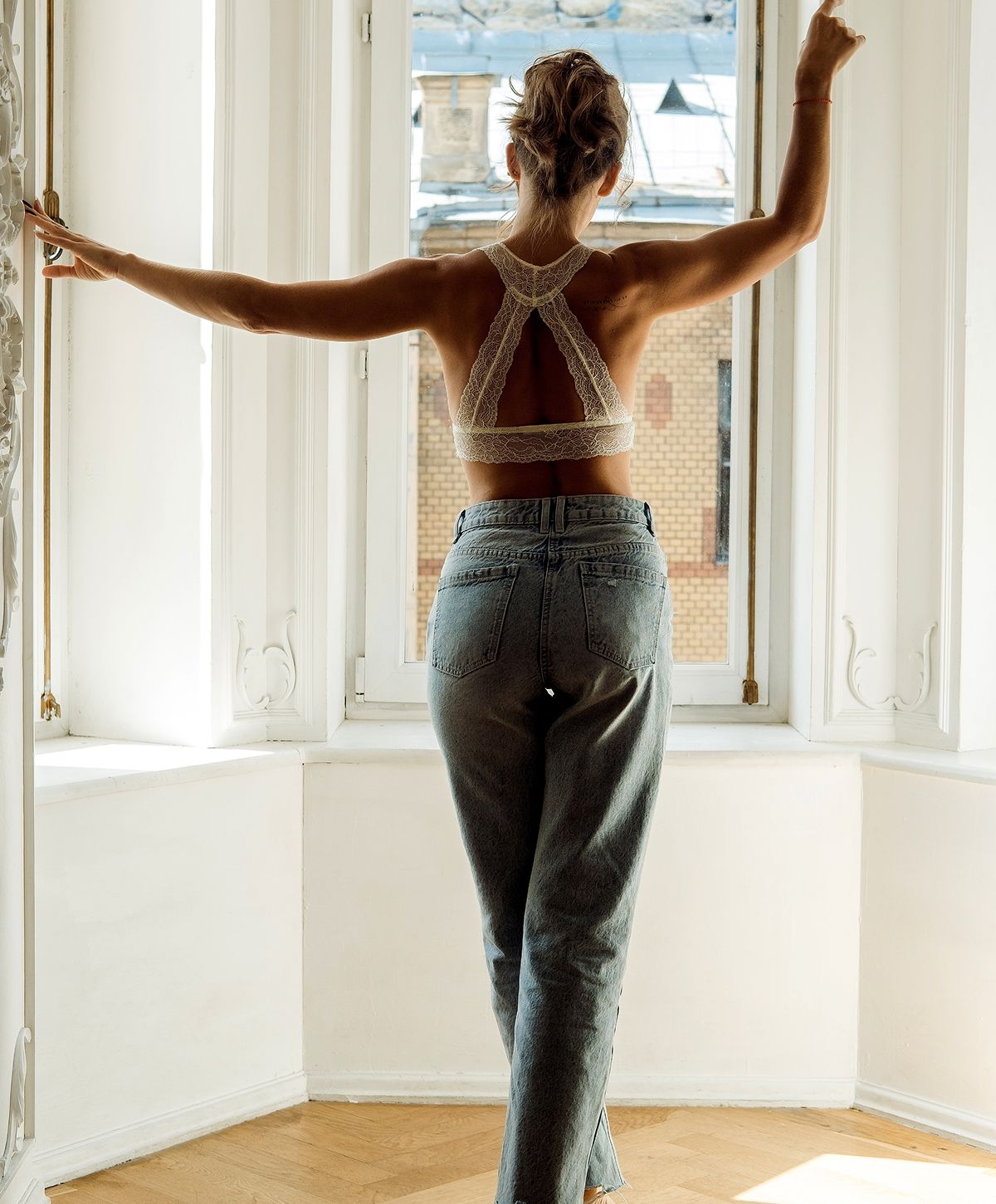 Woman in lace top by window, facing outside.