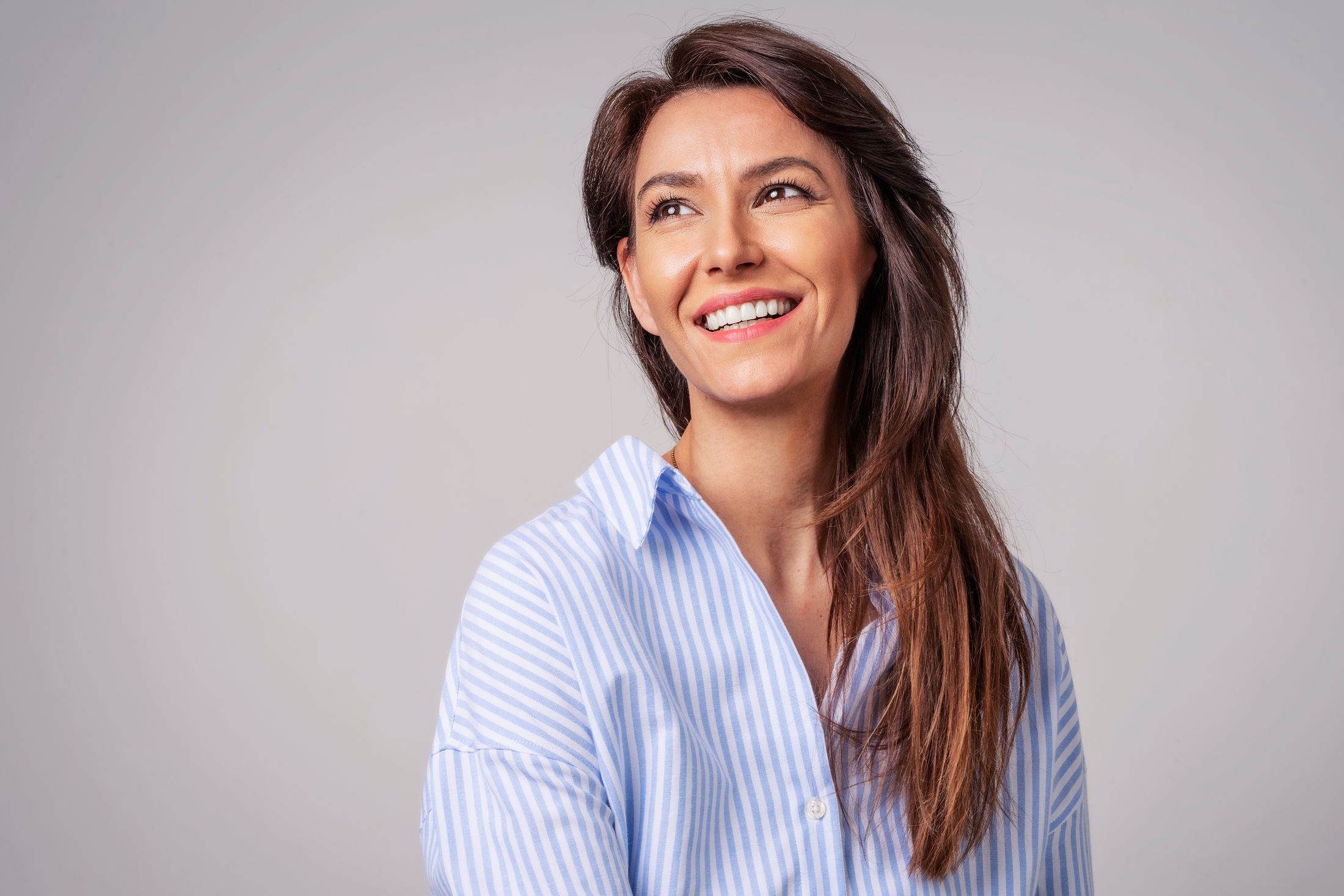 Smiling woman in striped shirt against gray background.