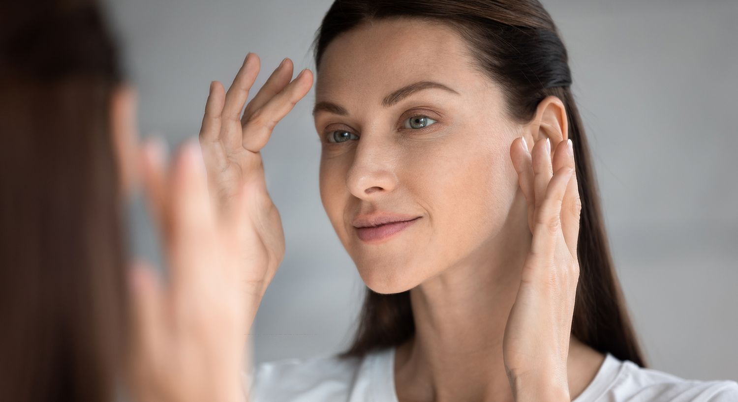Woman applying skincare in front of a mirror.
