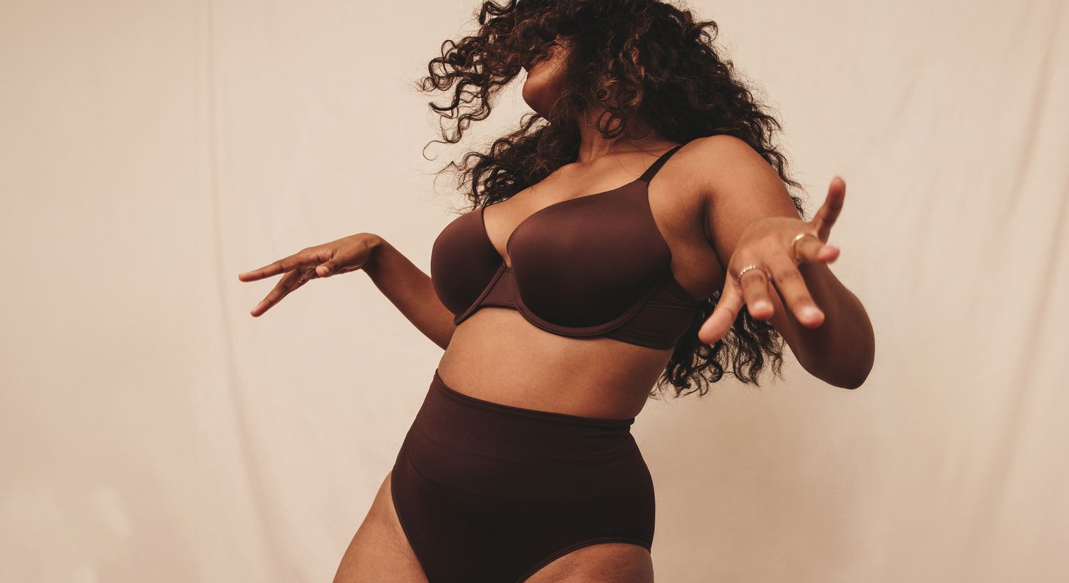 Person posing in brown lingerie against neutral background.